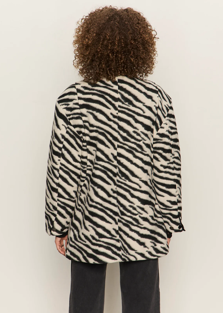 Woman turned around wearing a white and black zebra print barn jacket with black washed jeans against a white background