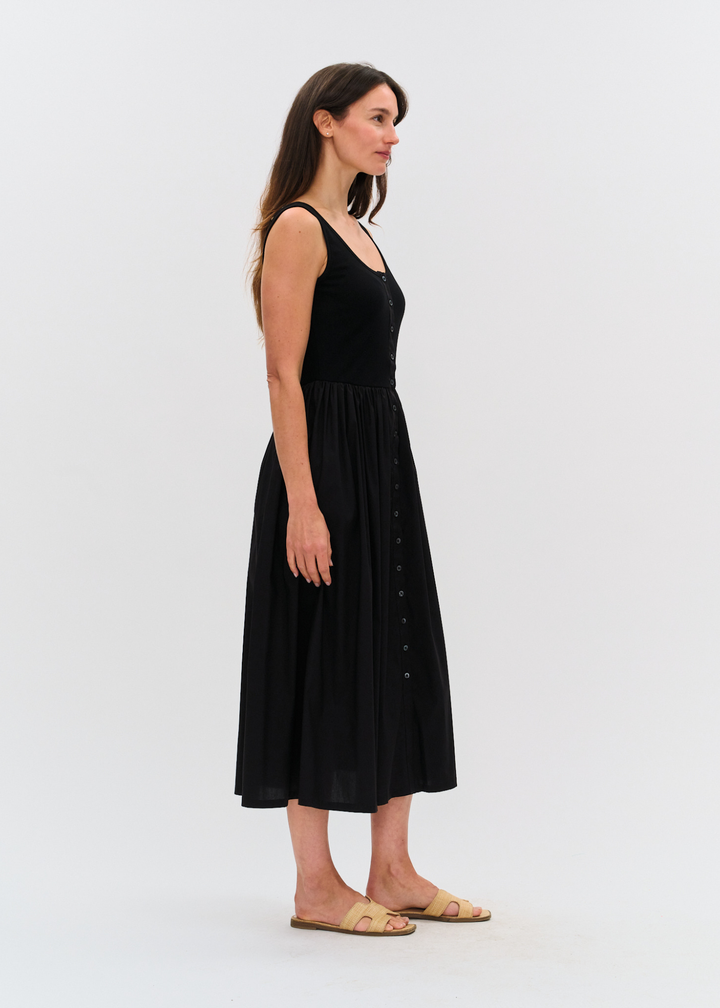 Woman turned to the side wearing a black midi dress with tan sandals