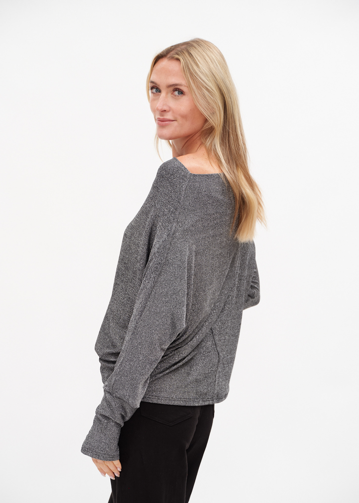 Woman turned to the side wearing a silver off the shoulder top with black jeans against a white background