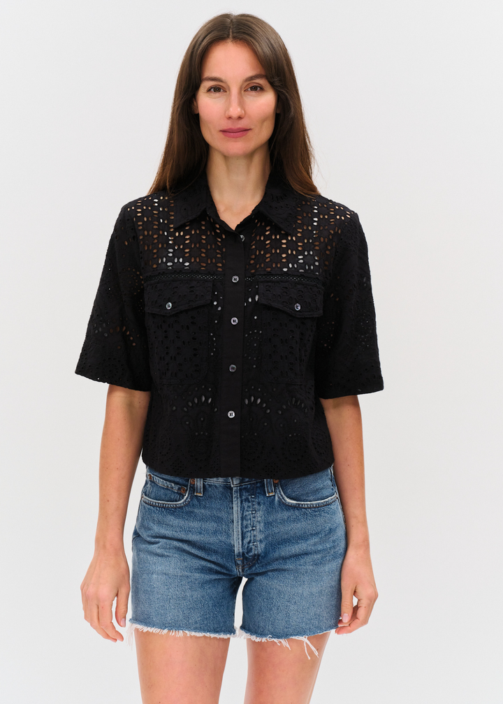 Woman wearing a black eyelet button down top with denim shorts