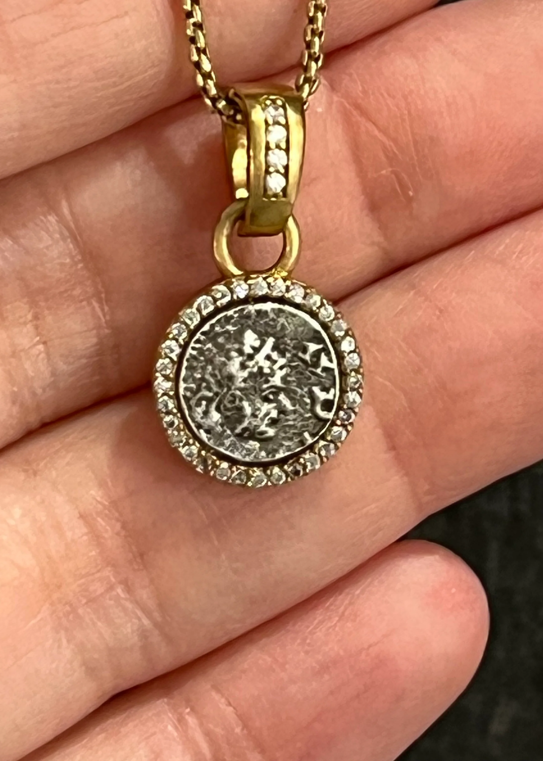 Woman holding a gold chain necklace with a silver coin pendant framed in gold and CZ pave