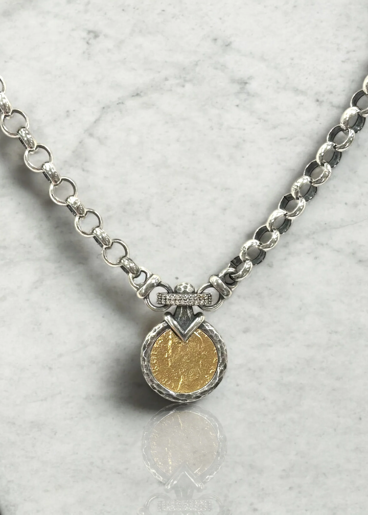 A vintage silver chain necklace with a gold coin pendant on a white background