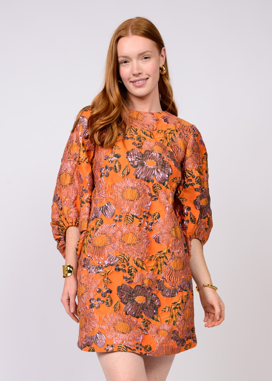 Woman wearing an orange mini dress with a floral pattern against a white background