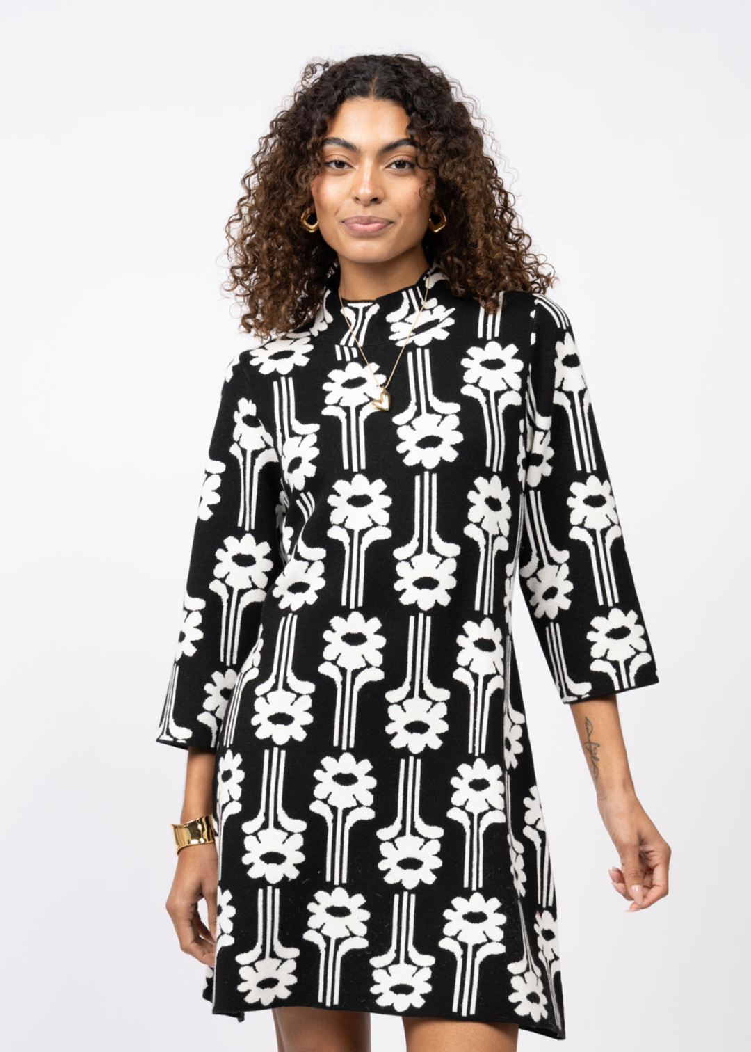 Woman wearing a black dress with a white pattern and 3/4 length sleeves in front of a white background