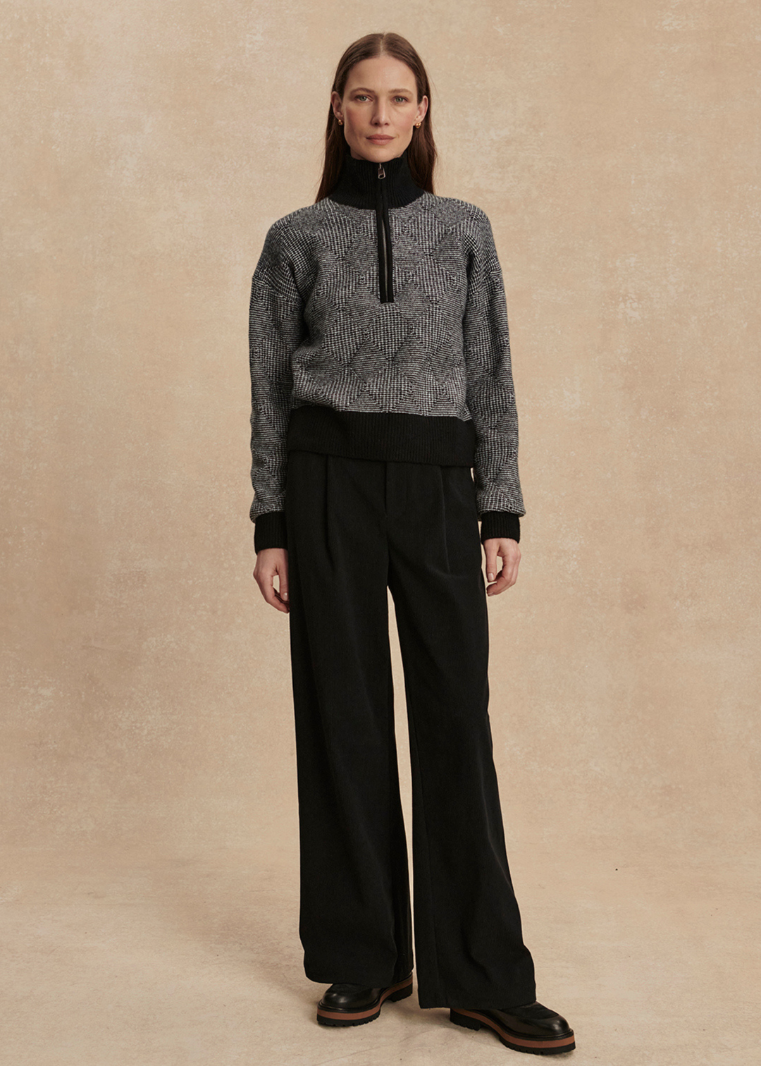 Woman wearing a black knit top with black pants against a tan background