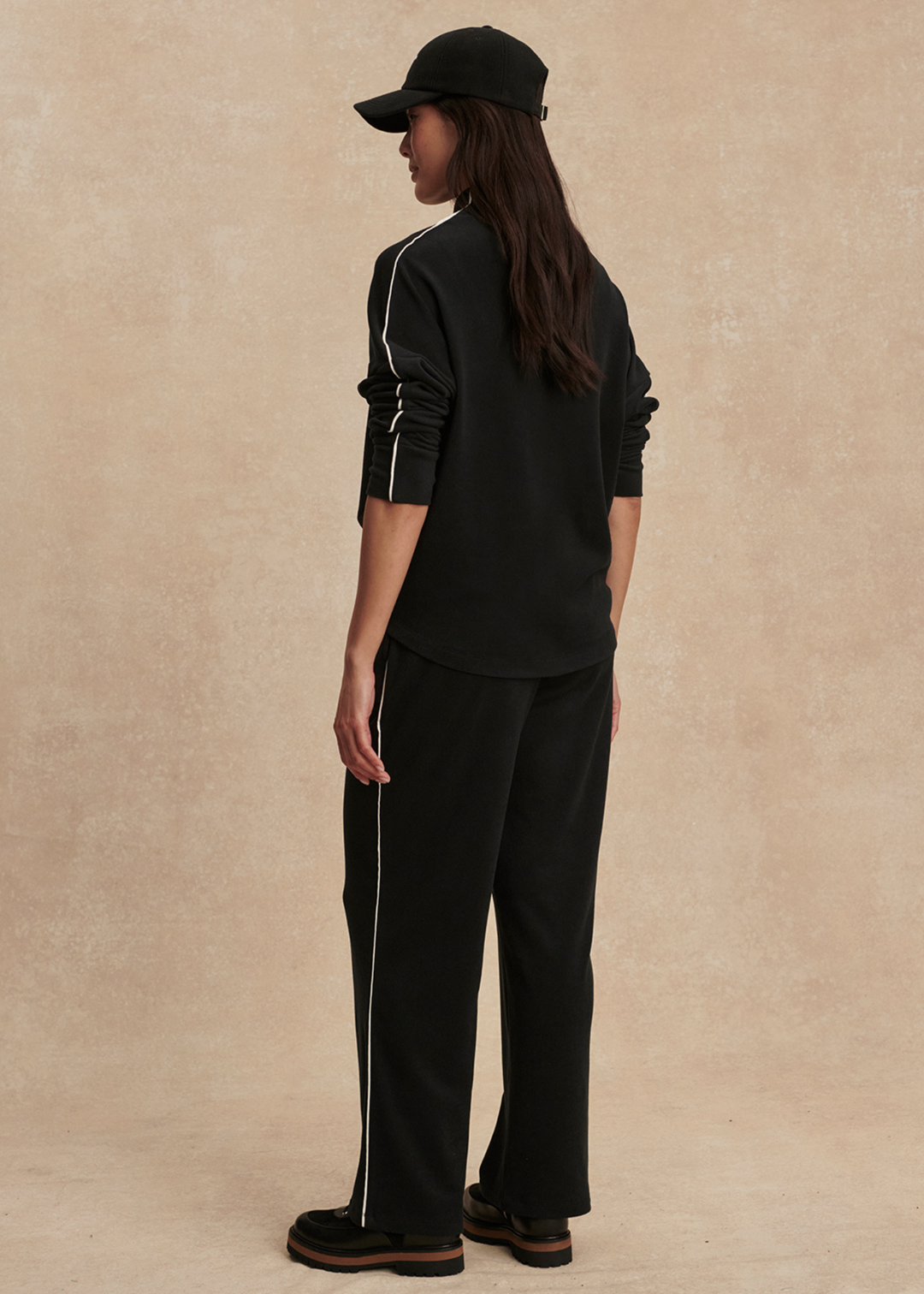 Woman turned to the side wearing a black top and black pants against a tan background