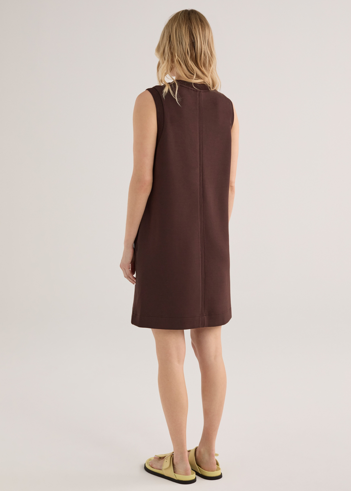 Woman turned around wearing a brown sleeveless mini dress with yellow sandals
