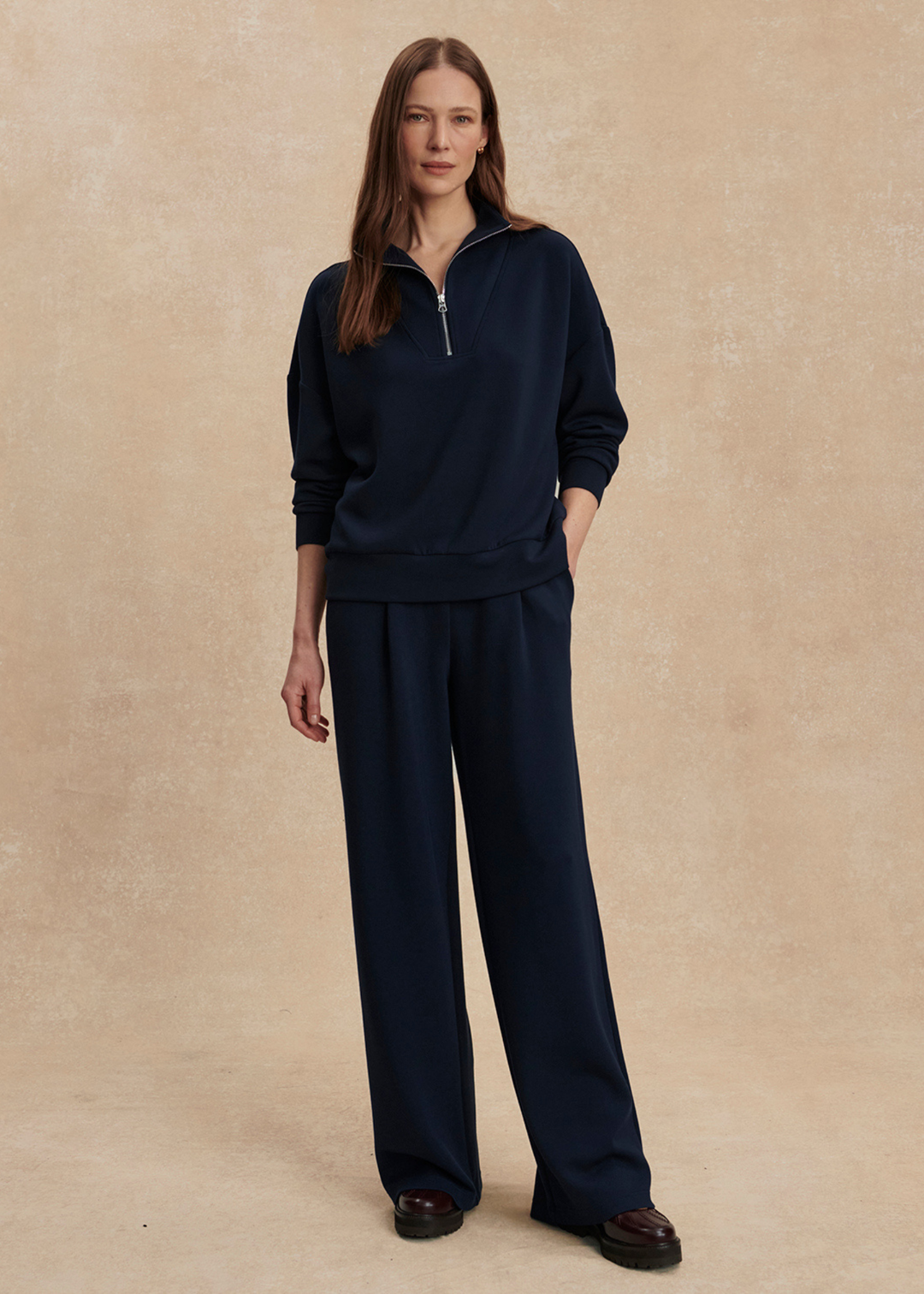 Woman wearing wide leg navy sweatpants with a matching top in front of a tan background