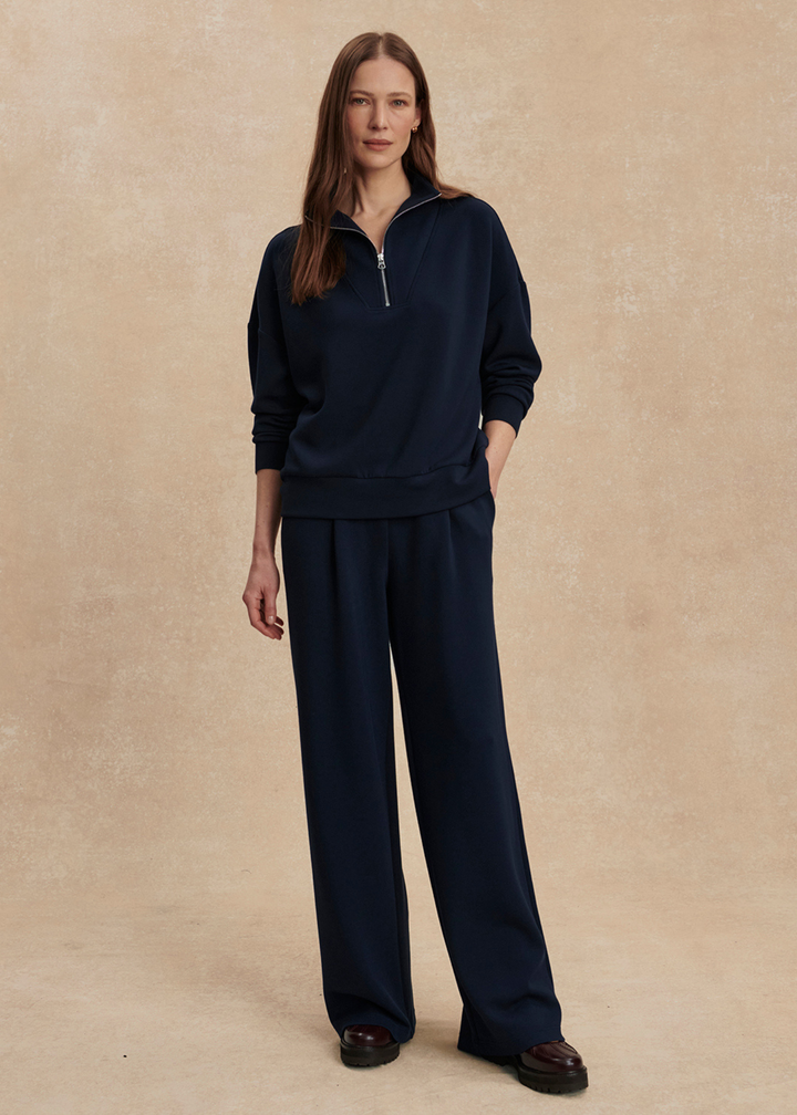 Woman wearing wide leg navy sweatpants with a matching top in front of a tan background
