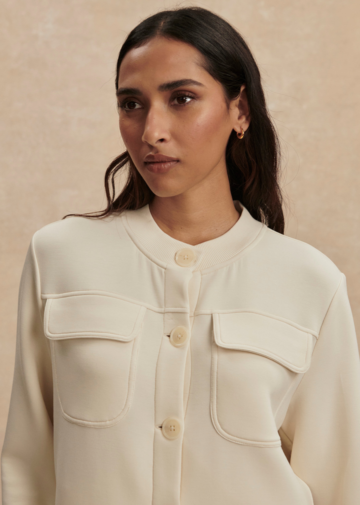 Close up of a woman wearing a cream button down sweater against a tan background