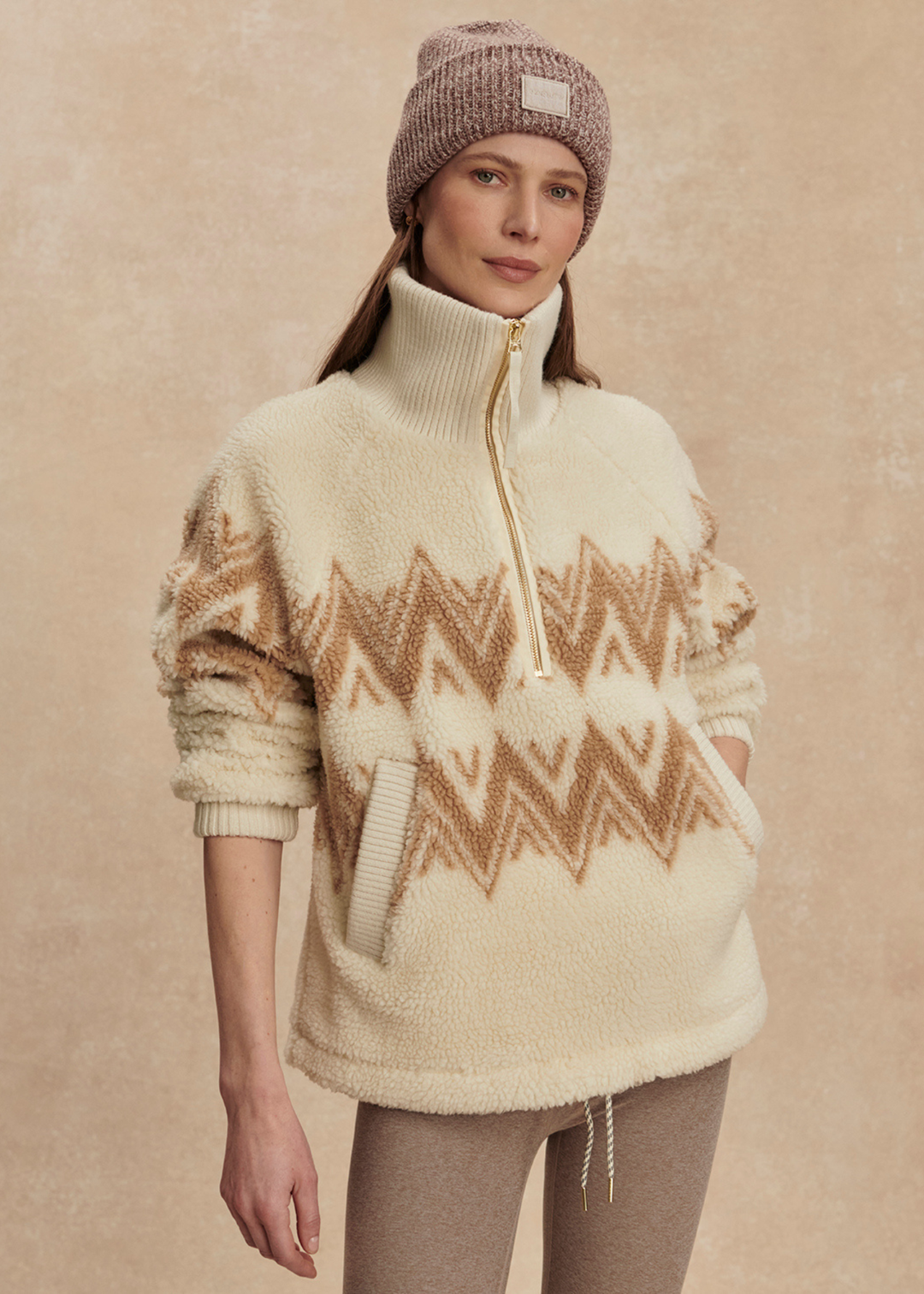 Woman wearing a cream and brown half zip sherpa with a brown beanie and leggings