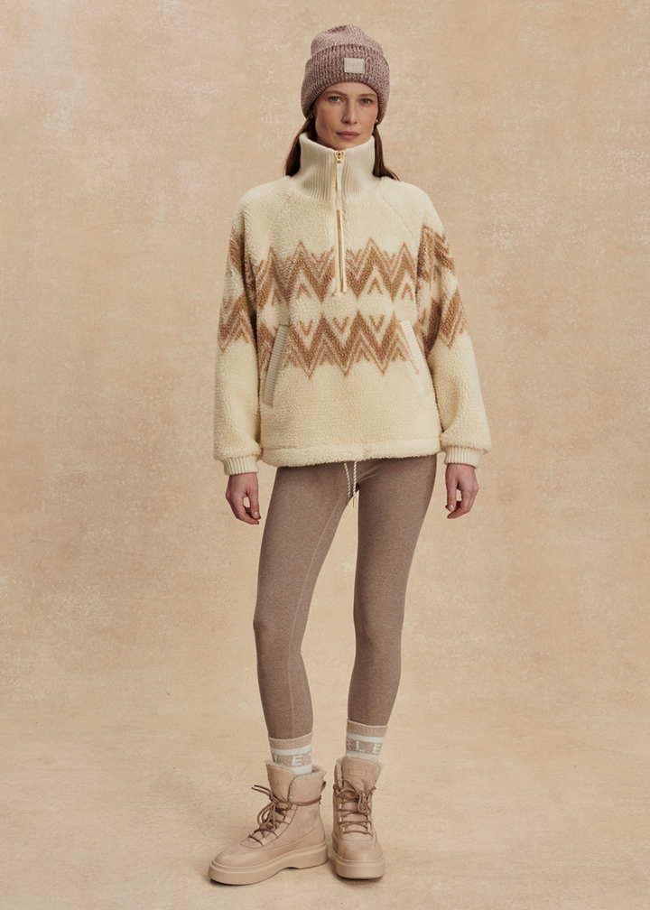 Woman wearing a cream and brown half zip sherpa with a brown beanie and leggings