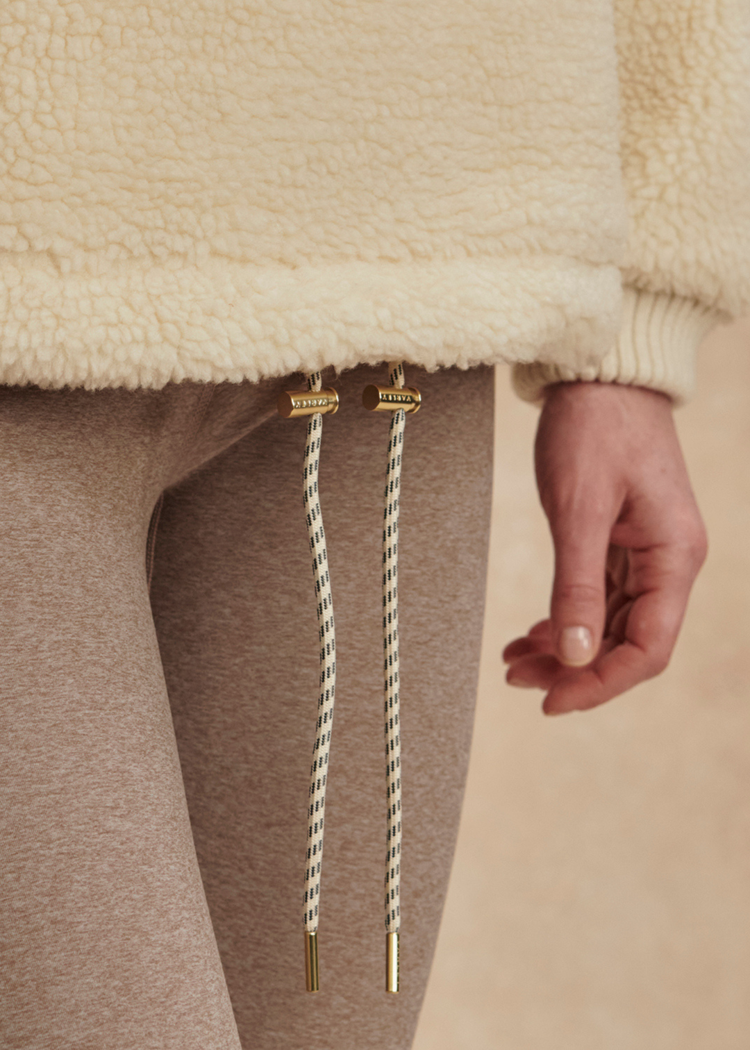 Close up of a woman wearing a cream sherpa with drawstrings and brown leggings