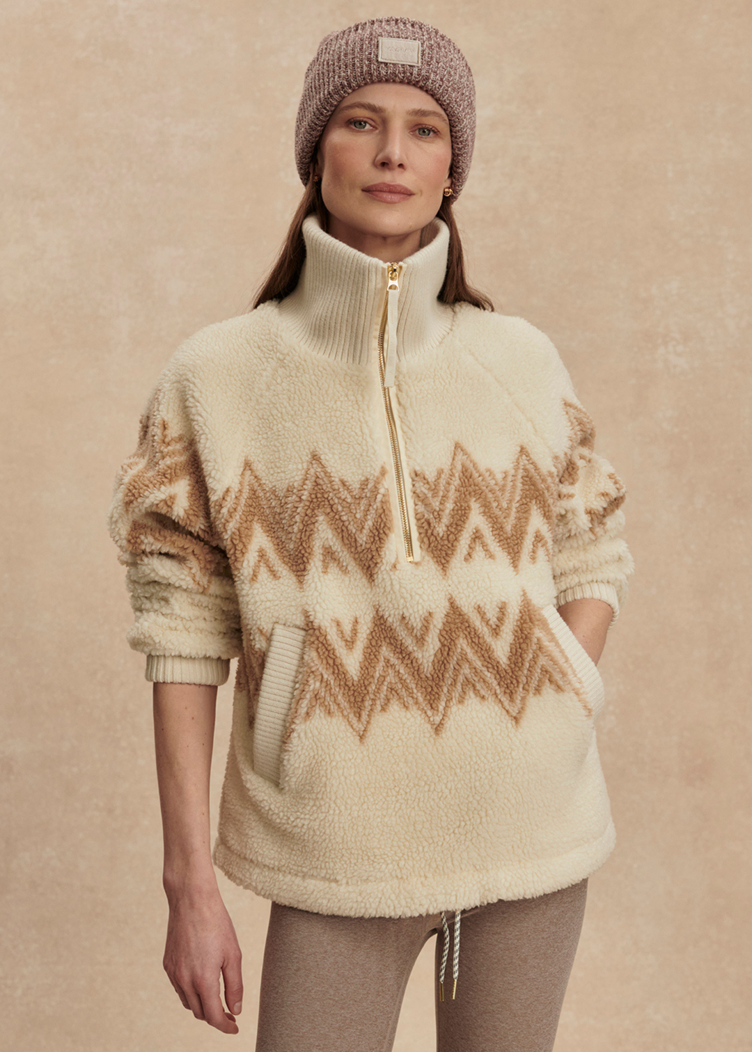 Woman wearing a cream and brown half zip sherpa with a brown beanie and leggings with hand in pocket
