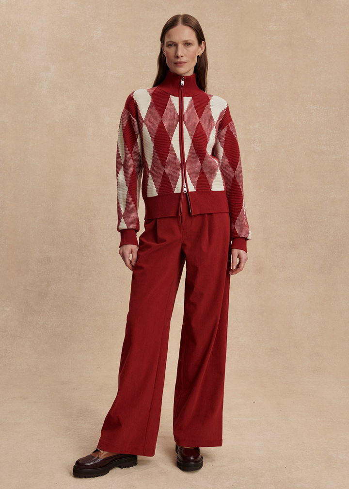 Woman wearing a red and white patterned sweater with red pants against a tan background