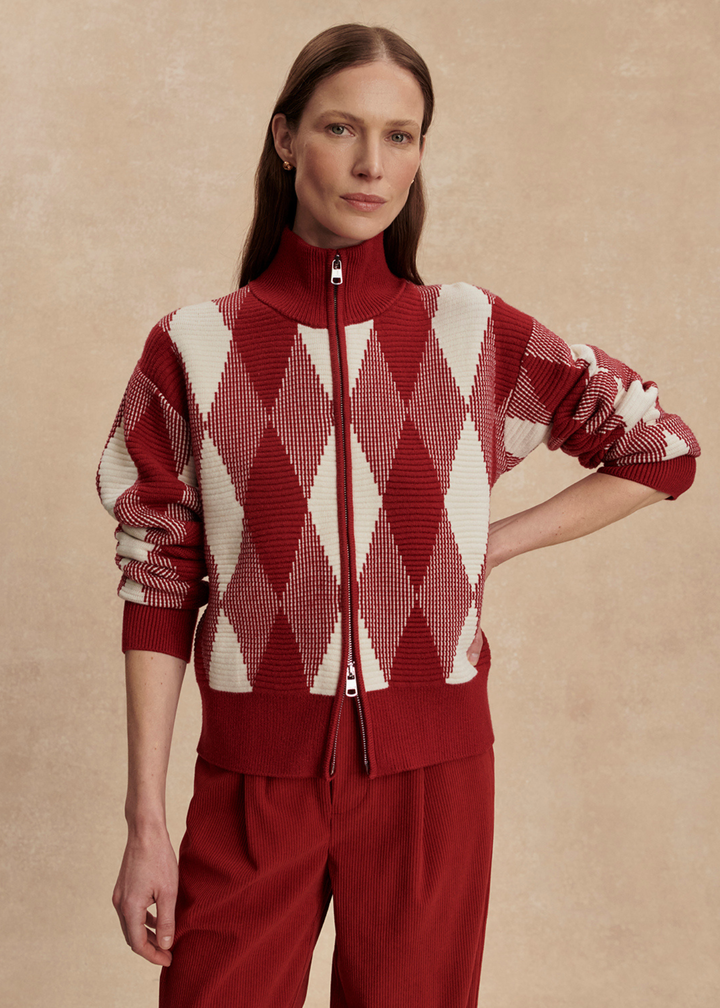 Woman wearing a red and white patterned sweater with red pants against a tan background