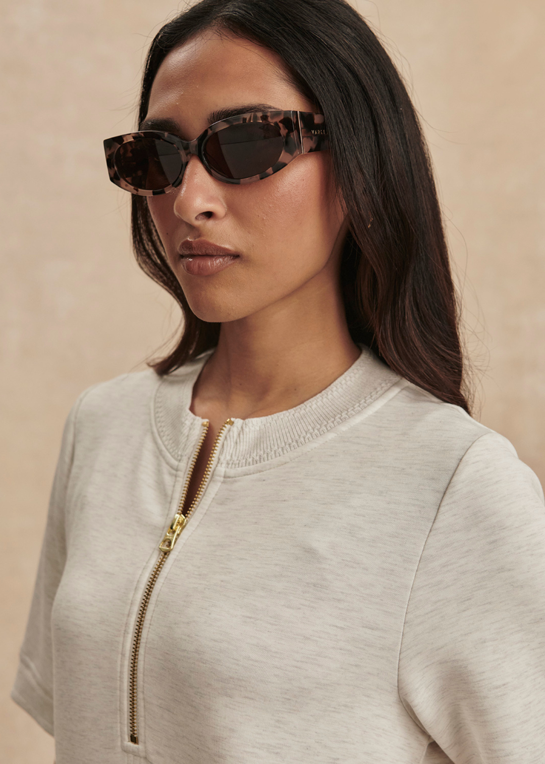 Close up of a woman wearing an ivory half zip mini dress with sunglasses