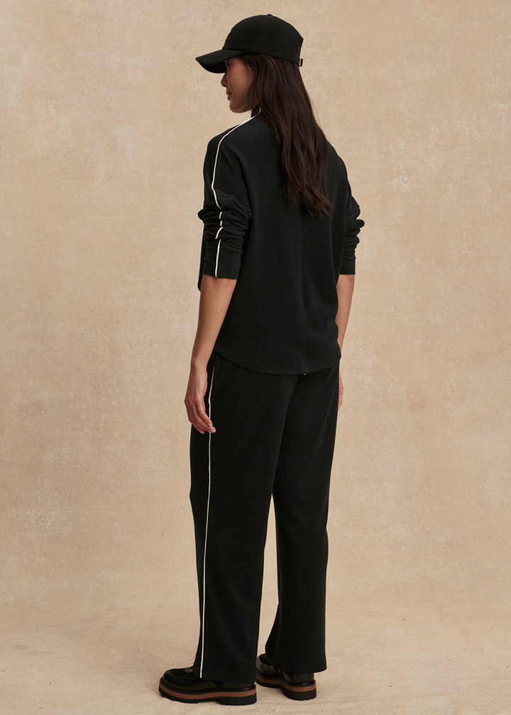 Woman turned to the side wearing a black set with white trim against a tan background