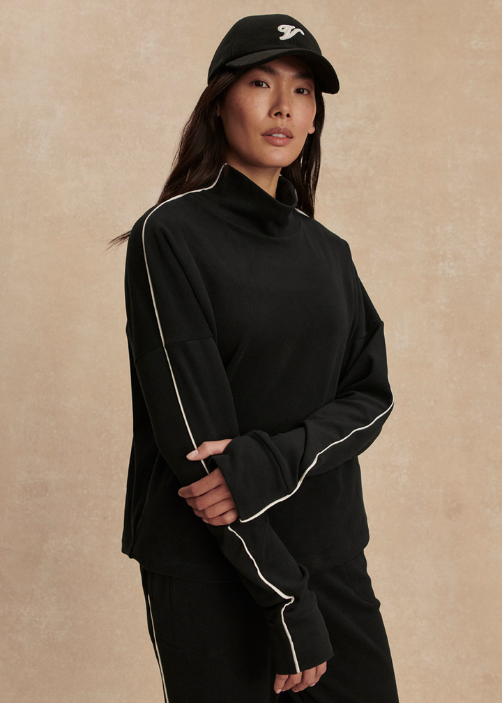 Woman wearing a black set with white trim against a tan background