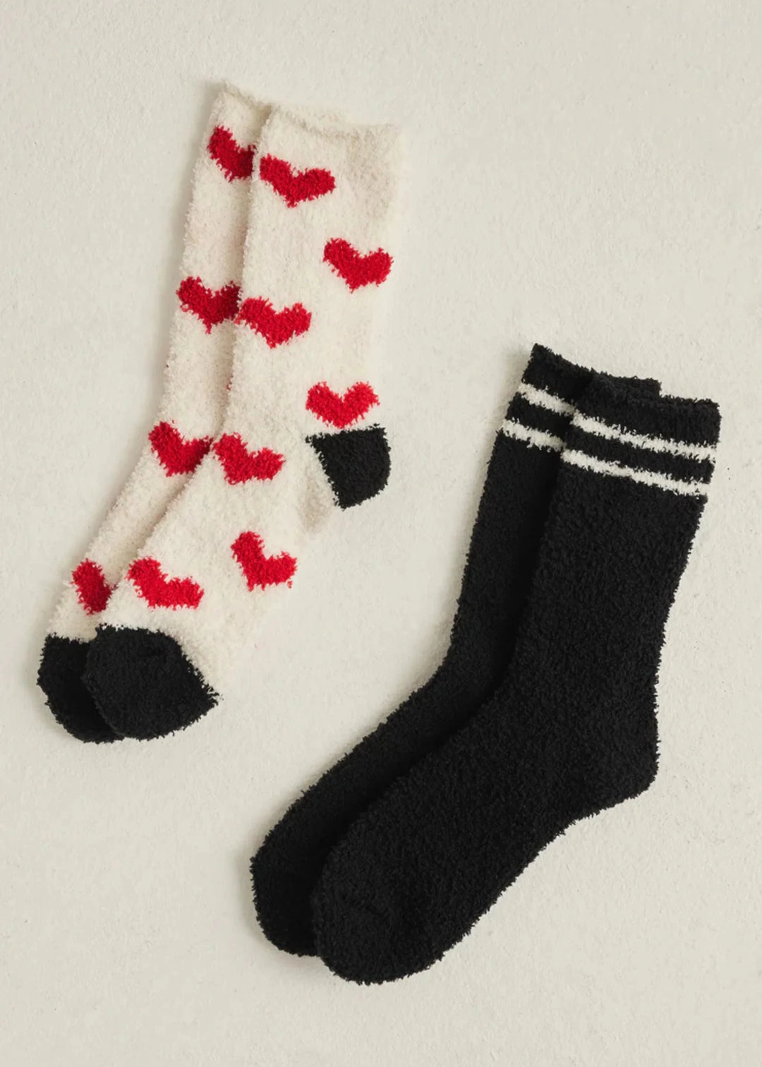 2 pack of socks one white pair with black toe and heel and red hearts all over, one black sock with white stripes 