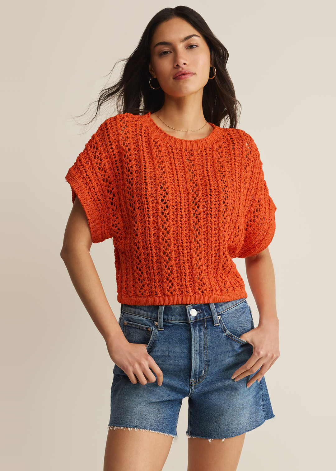 Woman wearing an orange crochet top with denim shorts