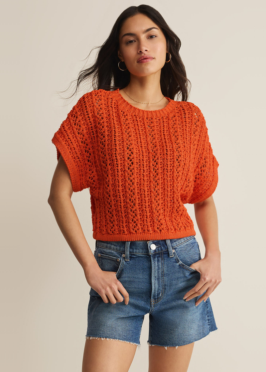 Woman wearing an orange crochet top with denim shorts