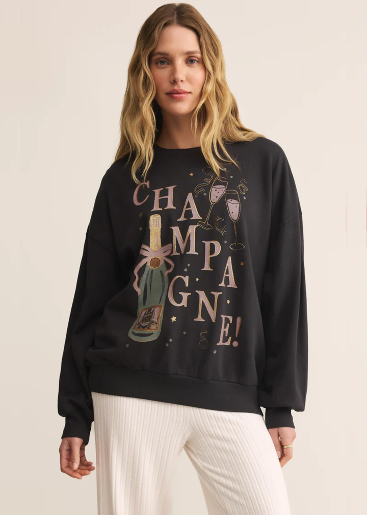 Woman wearing a grey sweatshirt with a champagne graphic and white pants