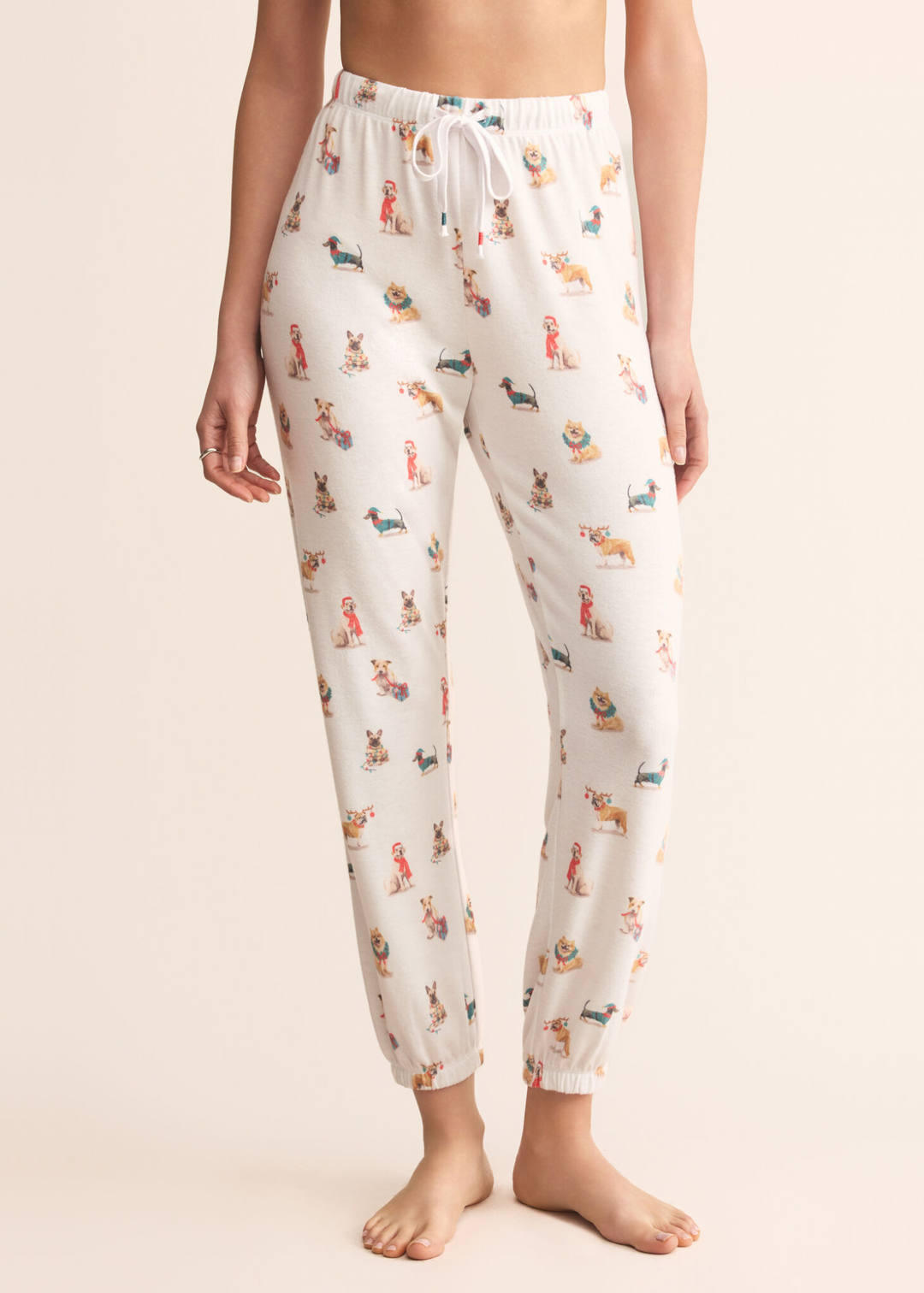 Woman wearing white joggers with a dog graphic pattern in front of a tan background