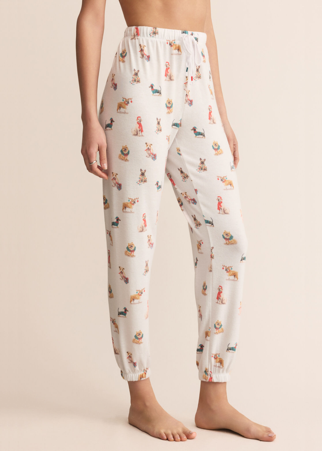 Woman turned to the side wearing white joggers with a dog graphic pattern in front of a tan background