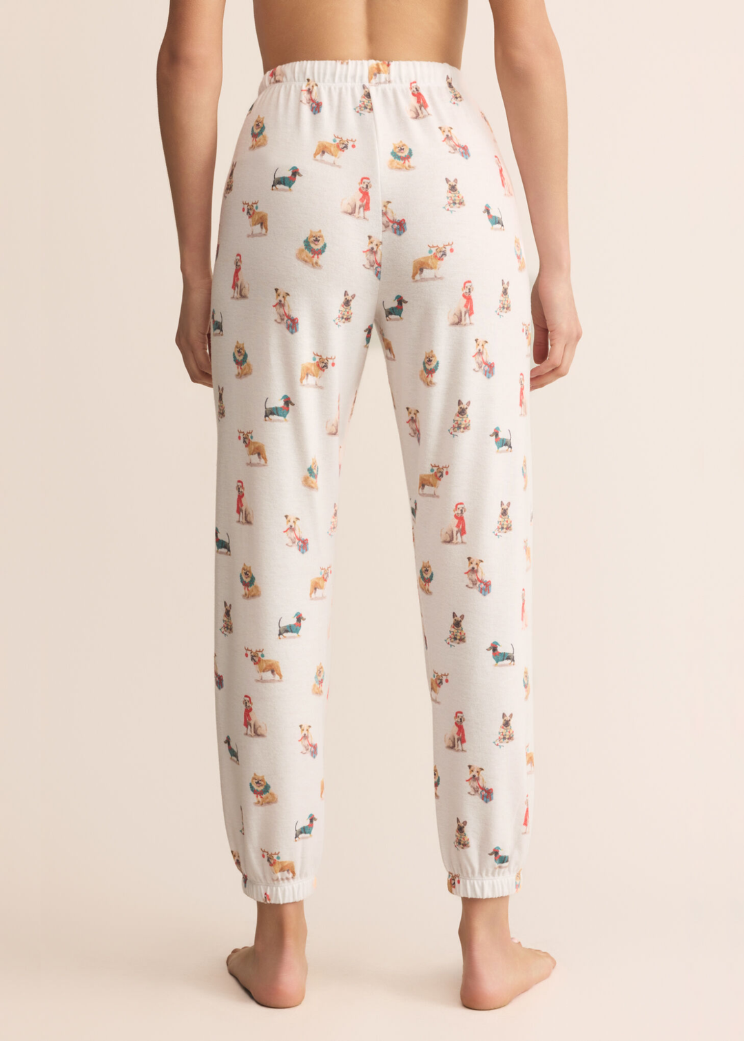 Woman turned around wearing white joggers with a dog graphic pattern in front of a tan background