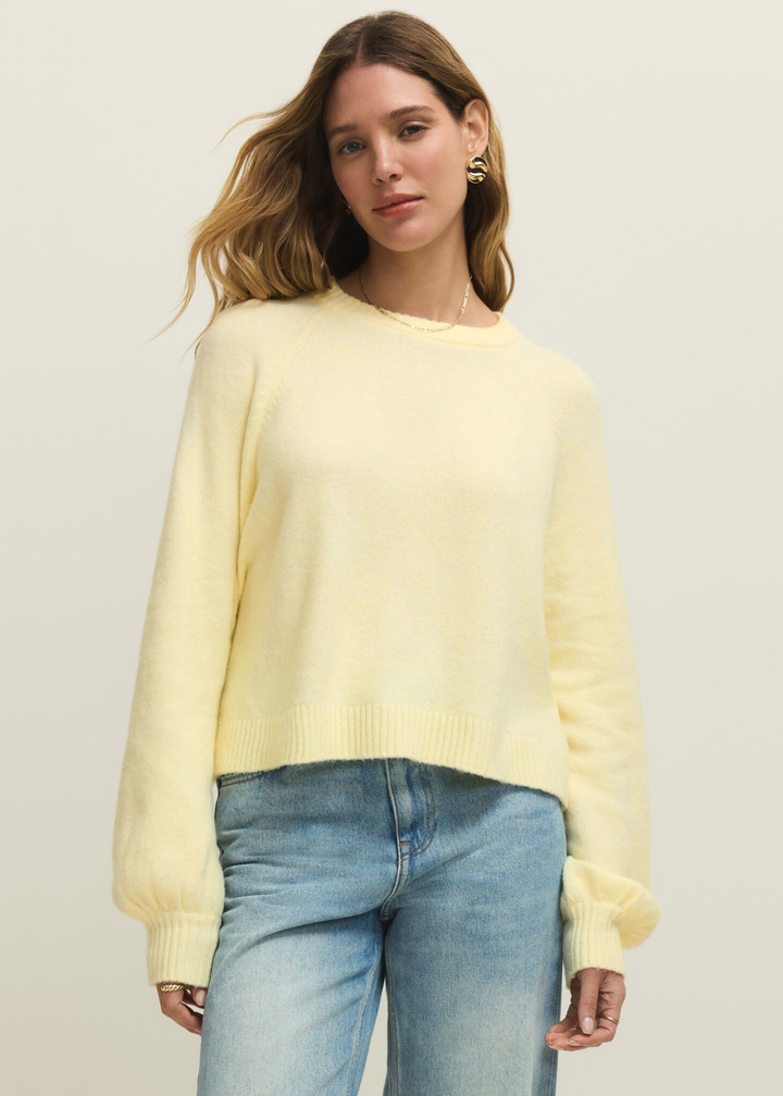 Woman wearing a light yellow sweater with jeans against a white background