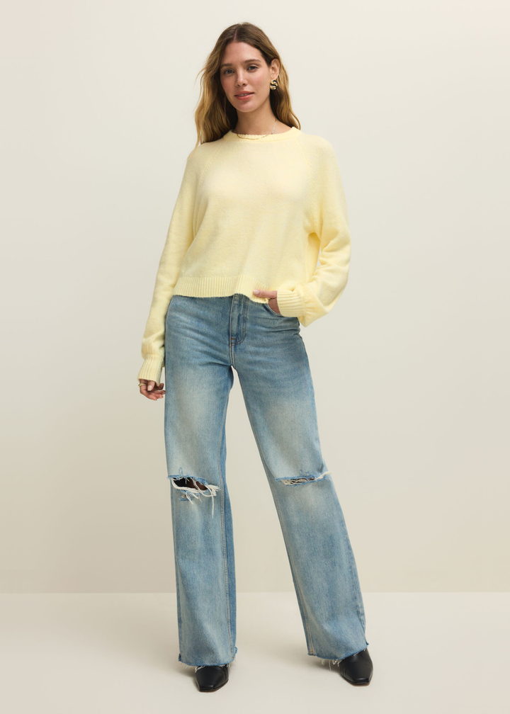 Woman wearing a light yellow sweater with jeans against a white background