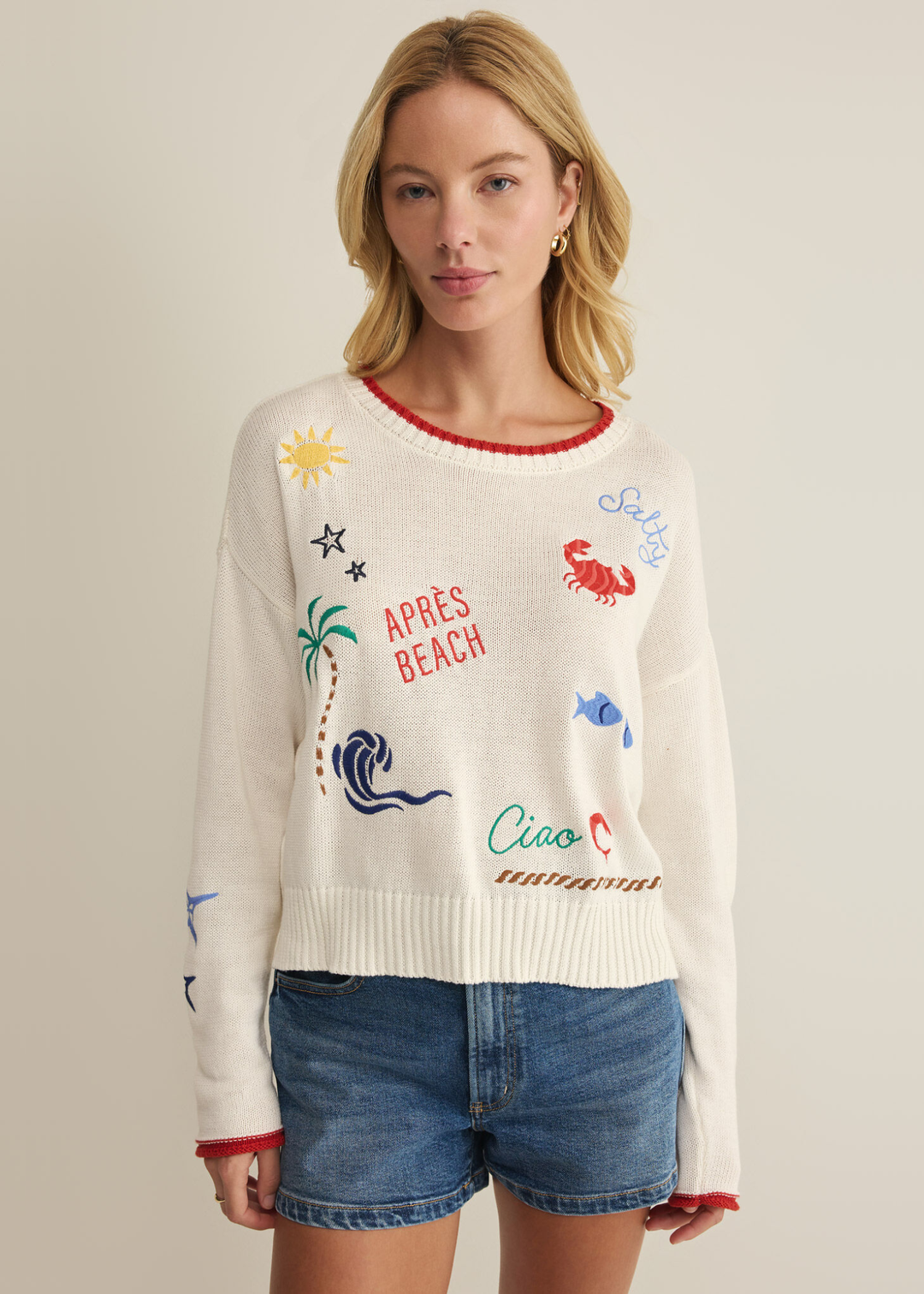 Woman wearing a white sweatshirt with multicolor embroidery and jean shorts
