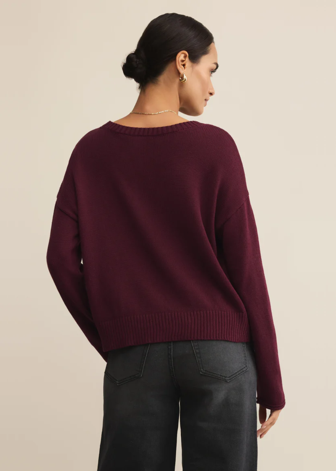 Woman turned around wearing a maroon sweater in front of a tan background