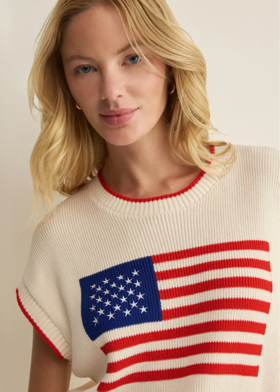 Woman wearing a cream sleeveless sweater with an American flag graphic 