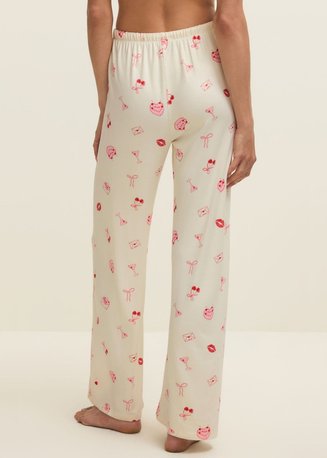 Woman turned around wearing white pajama pants with a pink and red graphic pattern