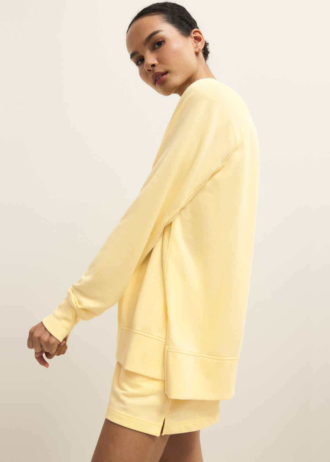 Woman turned to the side wearing a yellow v-neck sweatshirt with yellow shorts
