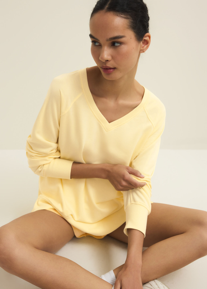 Woman sitting wearing a yellow v-neck sweatshirt with yellow shorts
