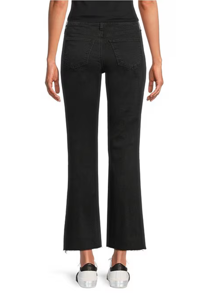Rear view of a model wearing black flared jeans with a cropped hem and frayed edges, paired with white sneakers, on a white background.