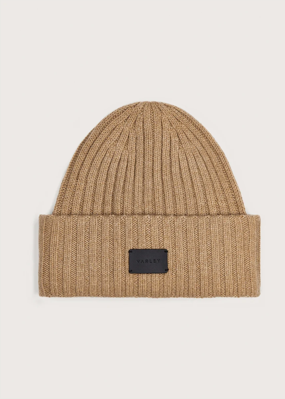A beige ribbed knit beanie hat with a folded cuff and a small black rectangular brand patch on the front, shown against a light gray background.