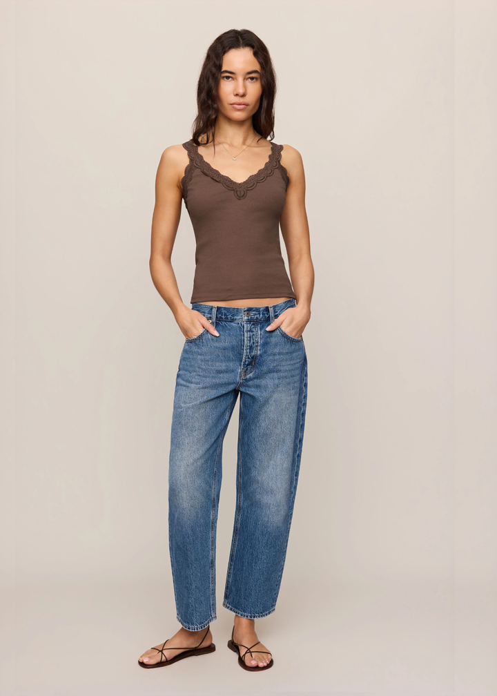A woman modeling a brown lace-trimmed sleeveless top and blue wide-leg jeans against a plain beige studio background.