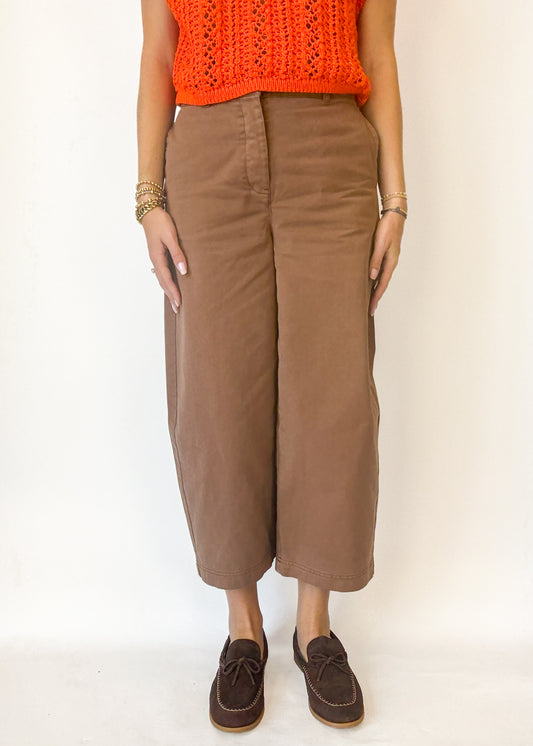 Person wearing brown wide-leg pants with an orange top on a white background