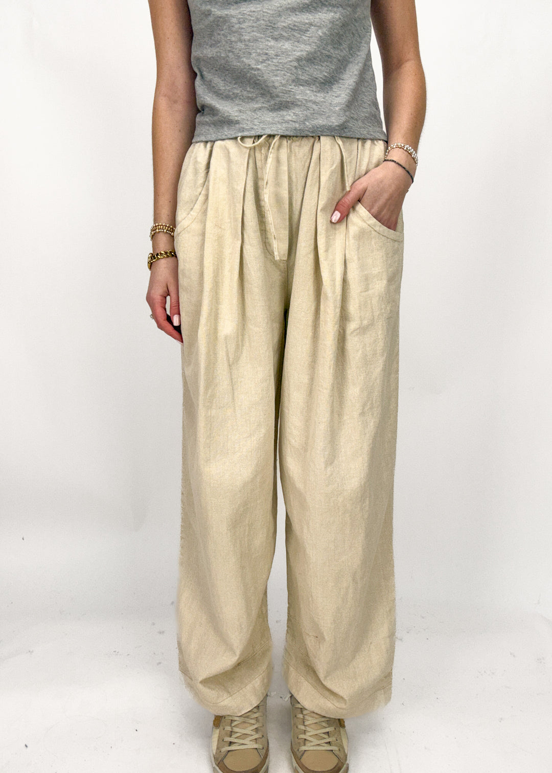 Person wearing beige wide-leg pants and a gray top on a white background