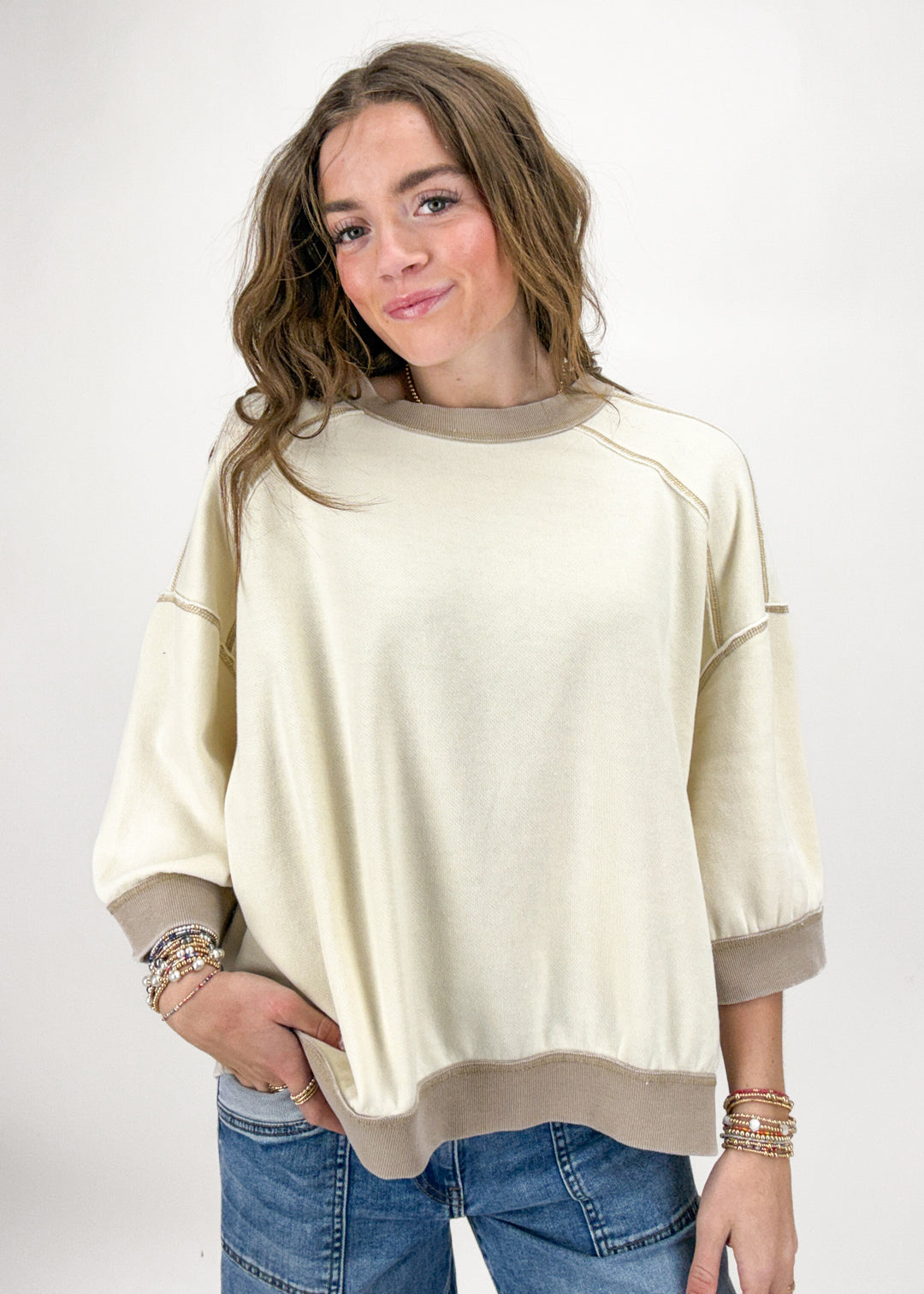 Woman wearing a beige sweater and blue jeans on a white background