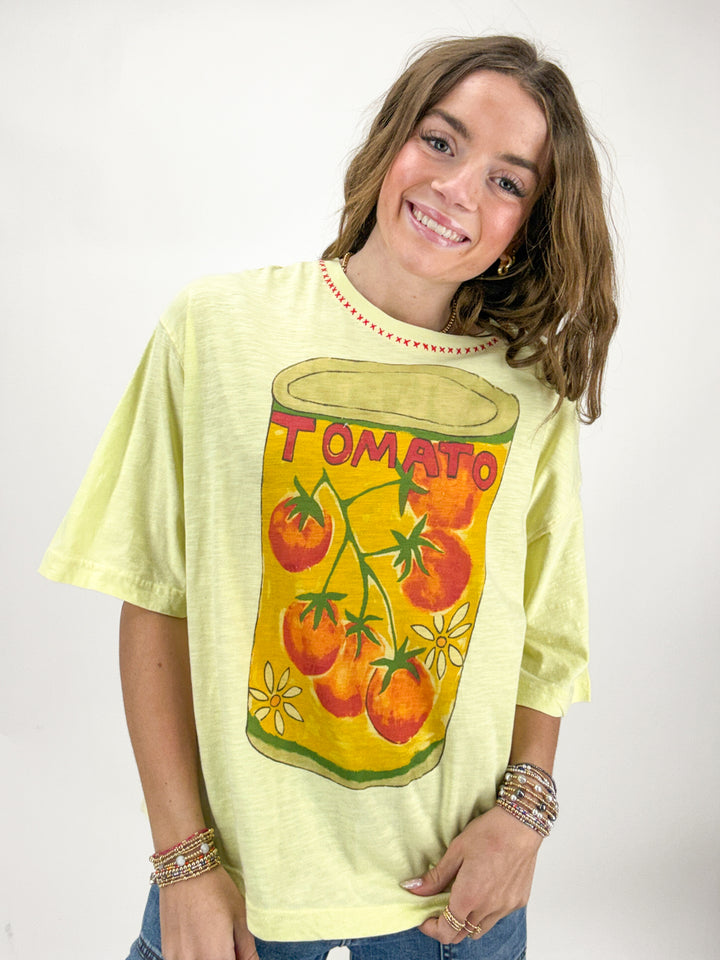 Person wearing a light green t-shirt with a tomato can graphic design on a white background