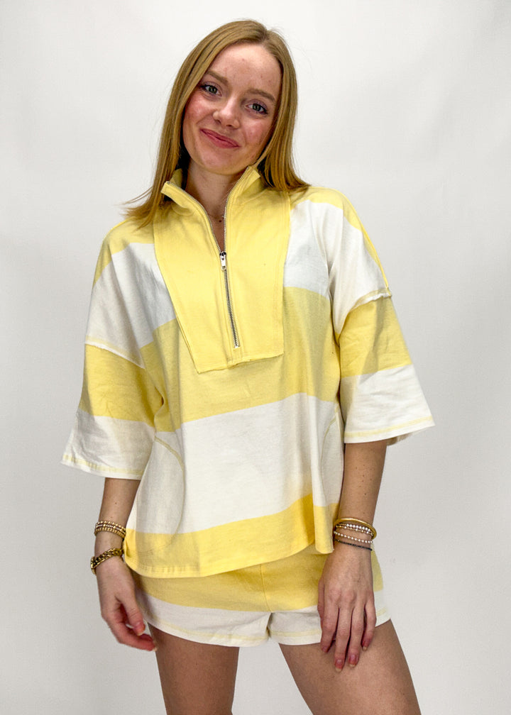 Woman wearing a yellow and white striped shirt with a quarter zip on a plain background