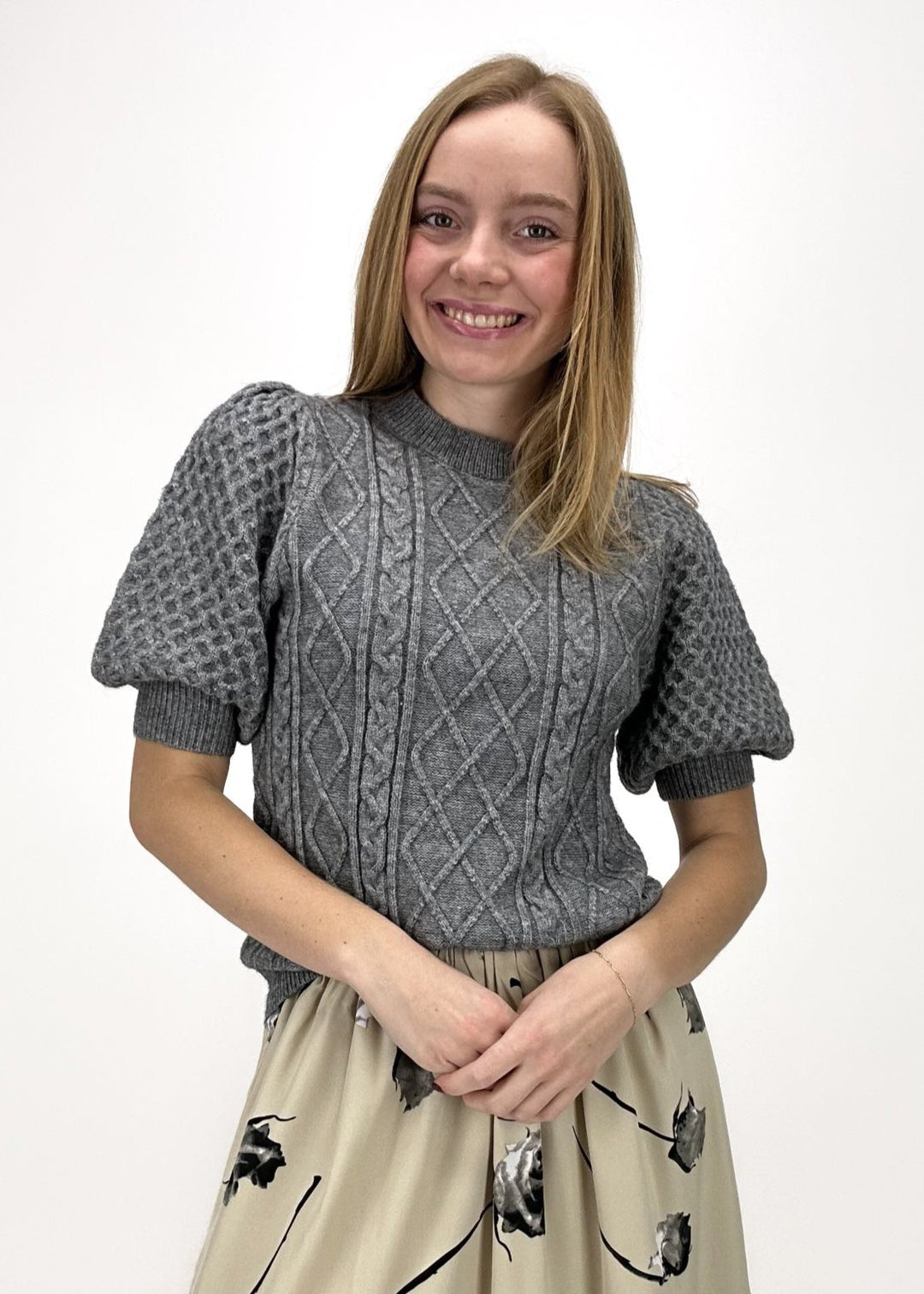 woman wearing medium grey cable knit short puff sleeve sweater top with tan and black rose printed tiered midi skirt