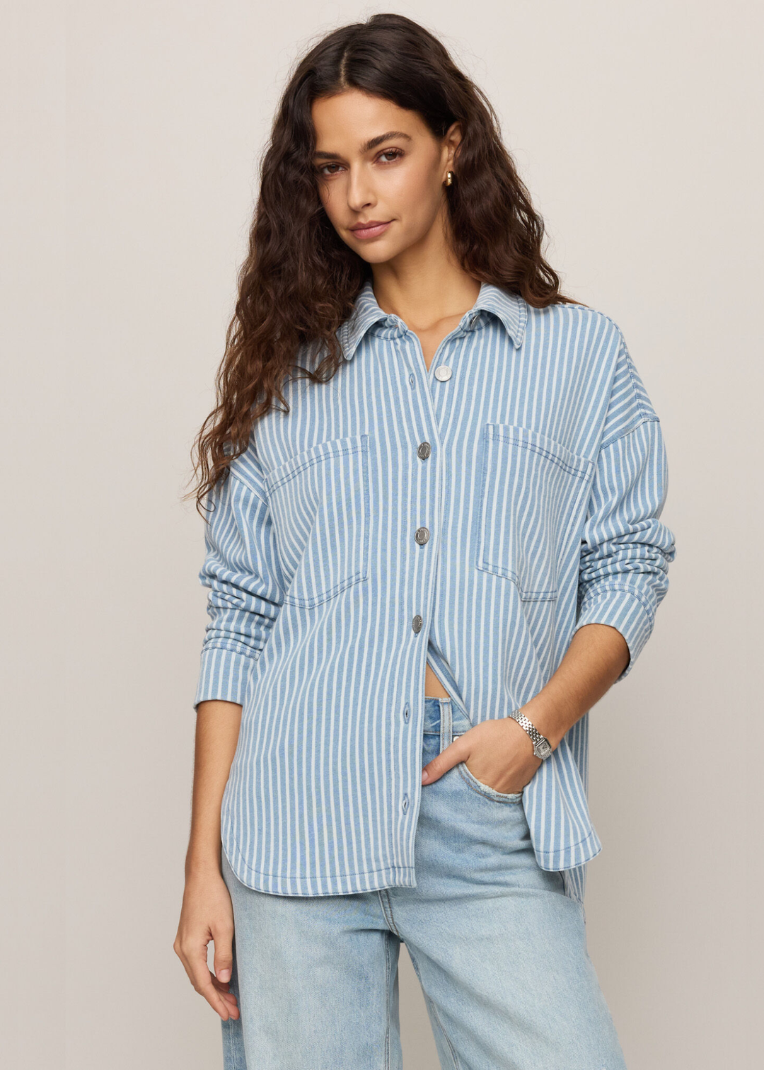 Woman wearing denim with white striped button down with hand in pocket. 
