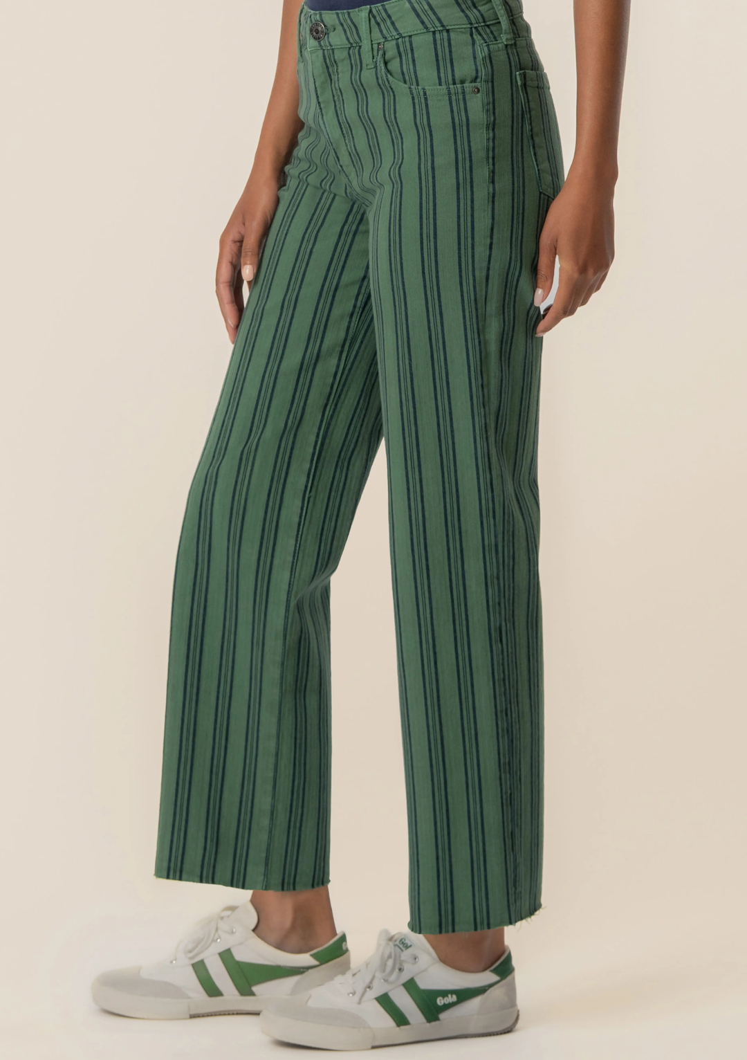 A person wearing green wide-leg cropped pants with thin dark vertical stripes, paired with white sneakers, shown against a plain light beige studio background.