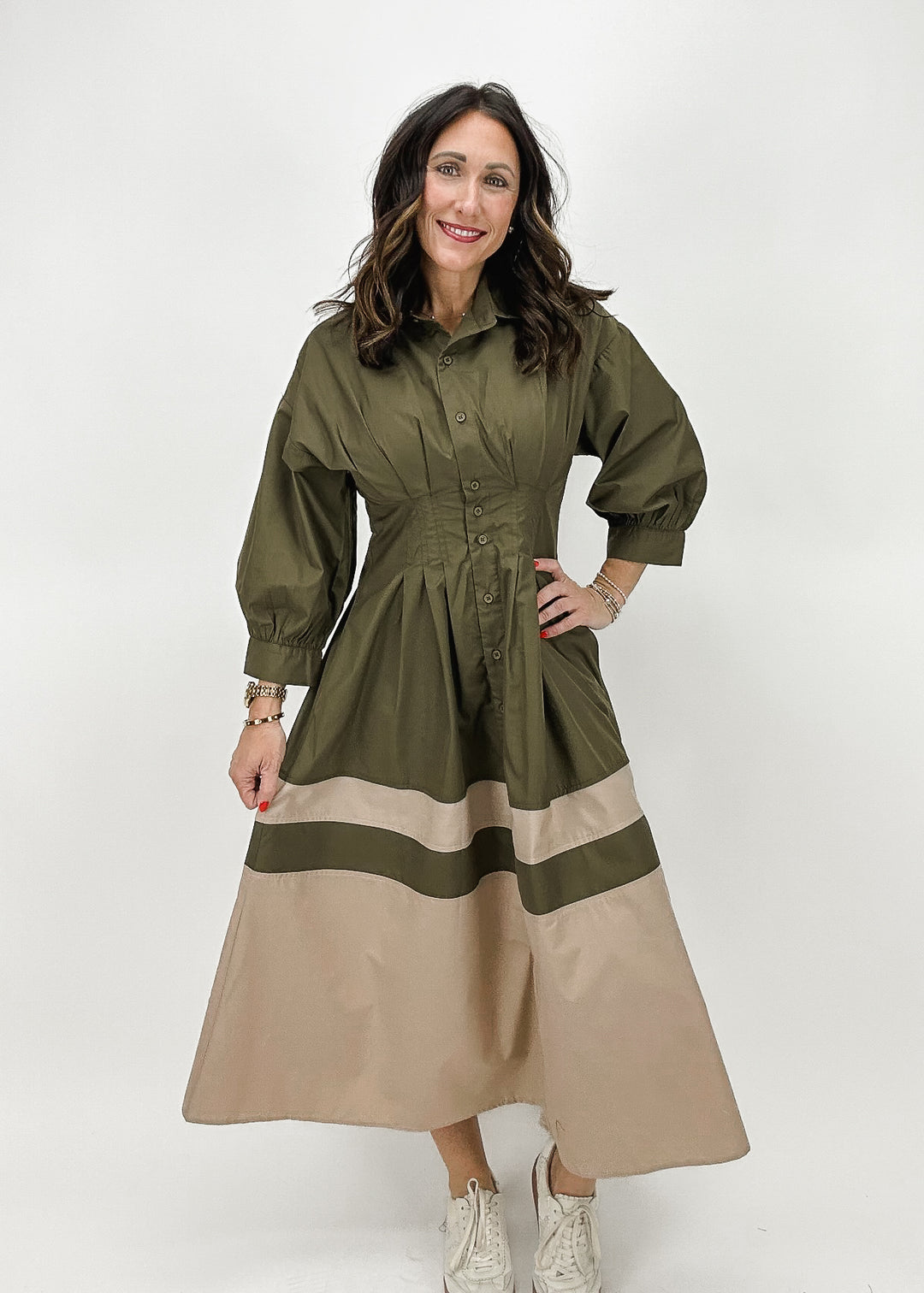 A woman wearing an olive green button-down midi dress with tan color blocks and a cinched waist, featuring a chic and structured silhouette.